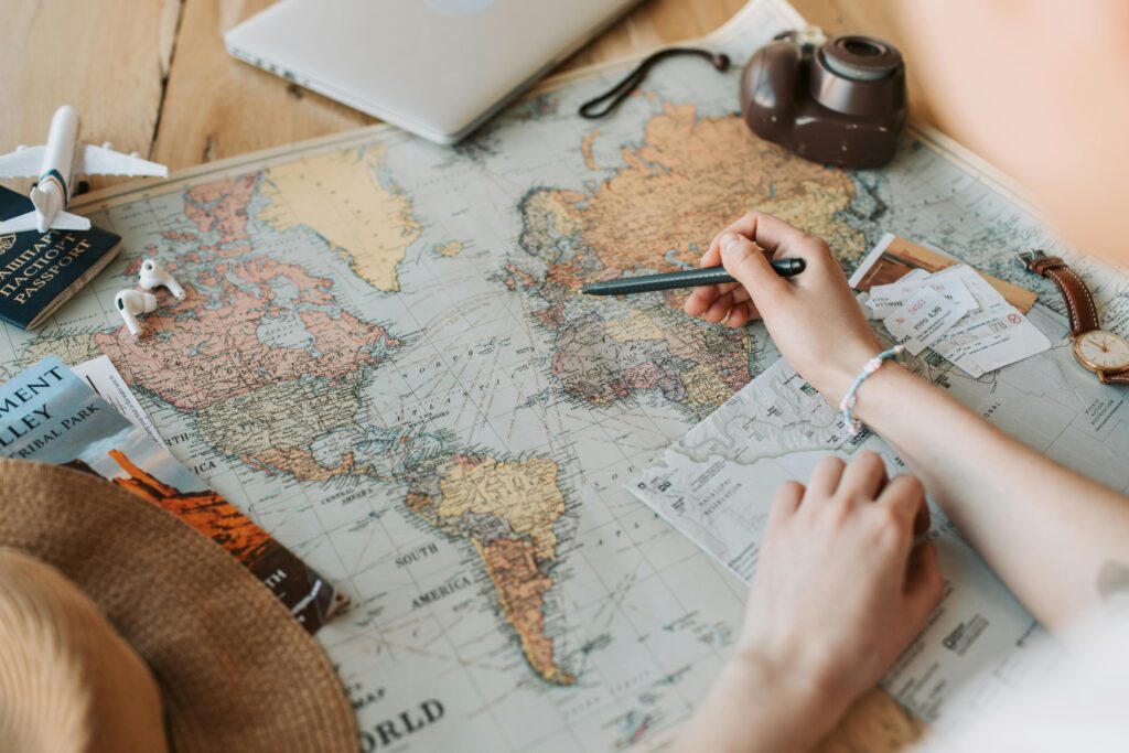 pexels-photo-7368308-7368308 Hands marking destinations on a world map surrounded by travel essentials like passport and camera.